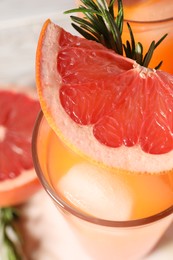 Tasty grapefruit drink with ice, rosemary and slice of fresh fruit in glass on table, closeup