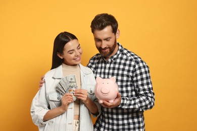 Photo of Happy couple with ceramic piggy bank and money on orange background