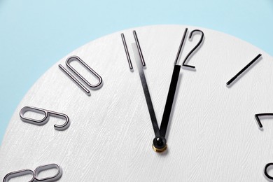 Stylish analog clock on light blue background, closeup. New Year countdown