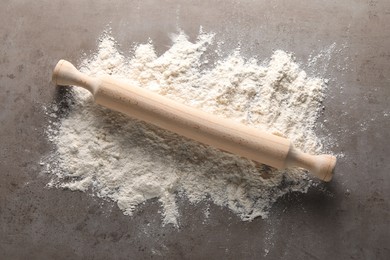 Scattered flour and rolling pin on grey textured table, top view