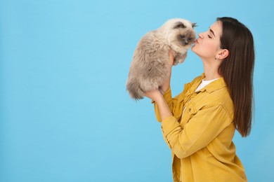 Photo of Woman kissing her cute cat on light blue background, space for text
