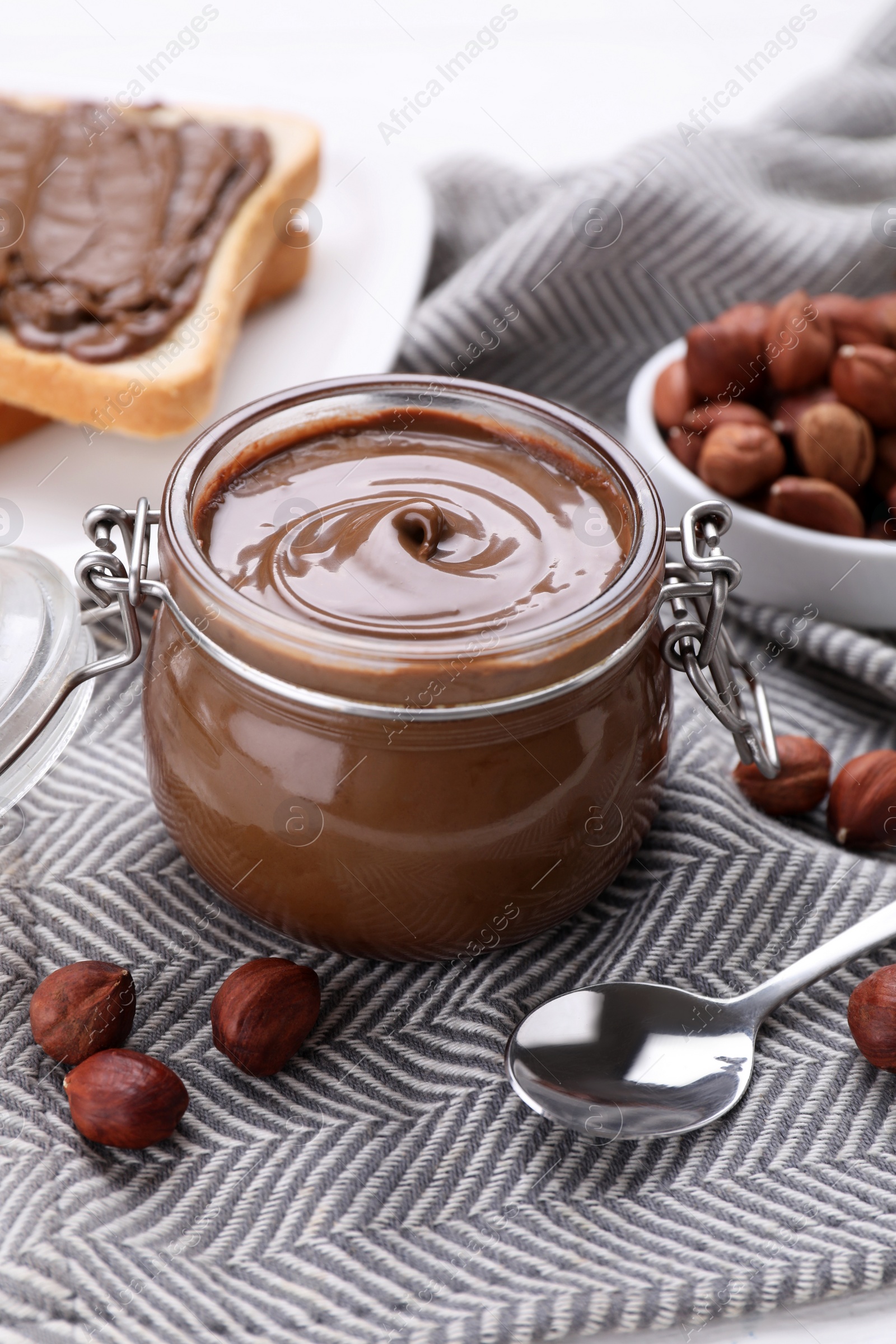 Photo of Jar with chocolate paste, tasty toast and nuts on table