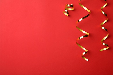 Photo of Shiny golden serpentine streamers on red background, flat lay. Space for text