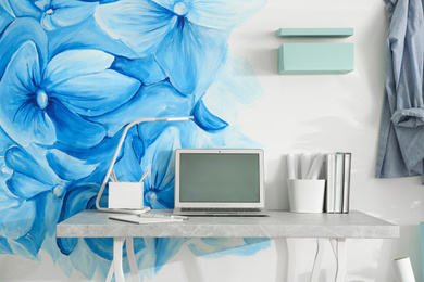 Photo of Stylish workplace with blue flowers painted on wall. Floral pattern in living room interior