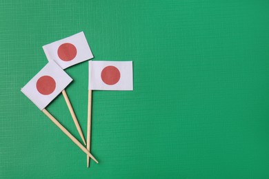 Small paper flags of Japan on green background, flat lay. Space for text