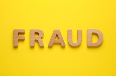 Word Fraud made of wooden letters on yellow background, flat lay