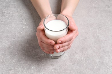 Photo of Woman holding glass of milk at light grey table, closeup