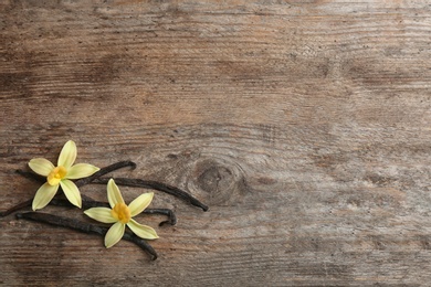 Photo of Flat lay composition with vanilla sticks and flowers on wooden background. Space for text
