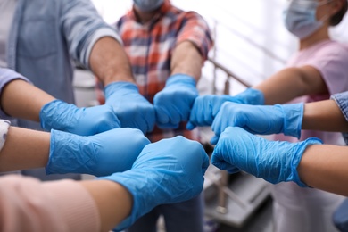 Photo of People in blue medical gloves joining fists indoors, closeup
