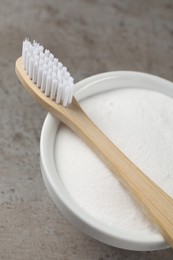 Bamboo toothbrush and bowl of baking soda on grey table, closeup