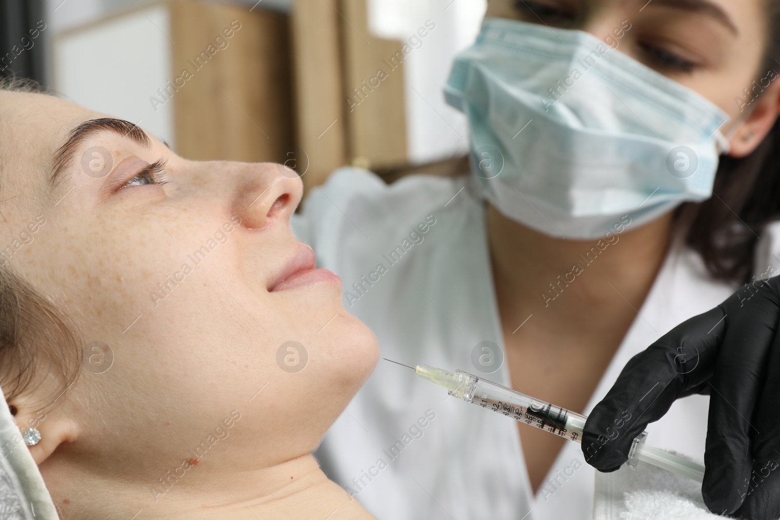 Photo of Cosmetologist giving facial injection to patient in clinic, selective focus. Cosmetic surgery