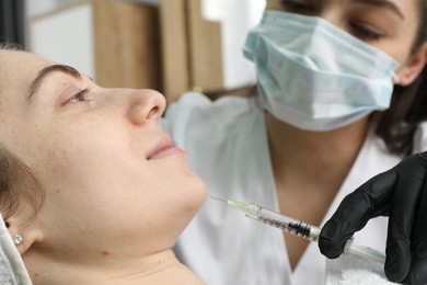 Photo of Cosmetologist giving facial injection to patient in clinic, selective focus. Cosmetic surgery