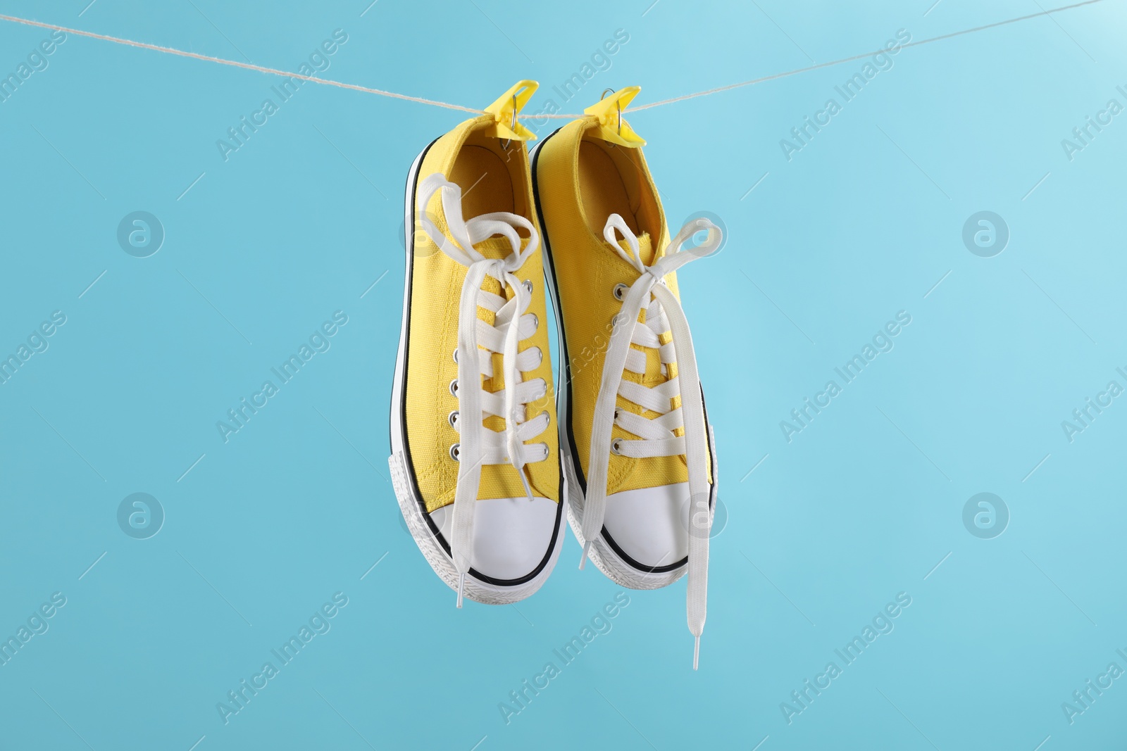 Photo of Stylish sneakers drying on washing line against light blue background