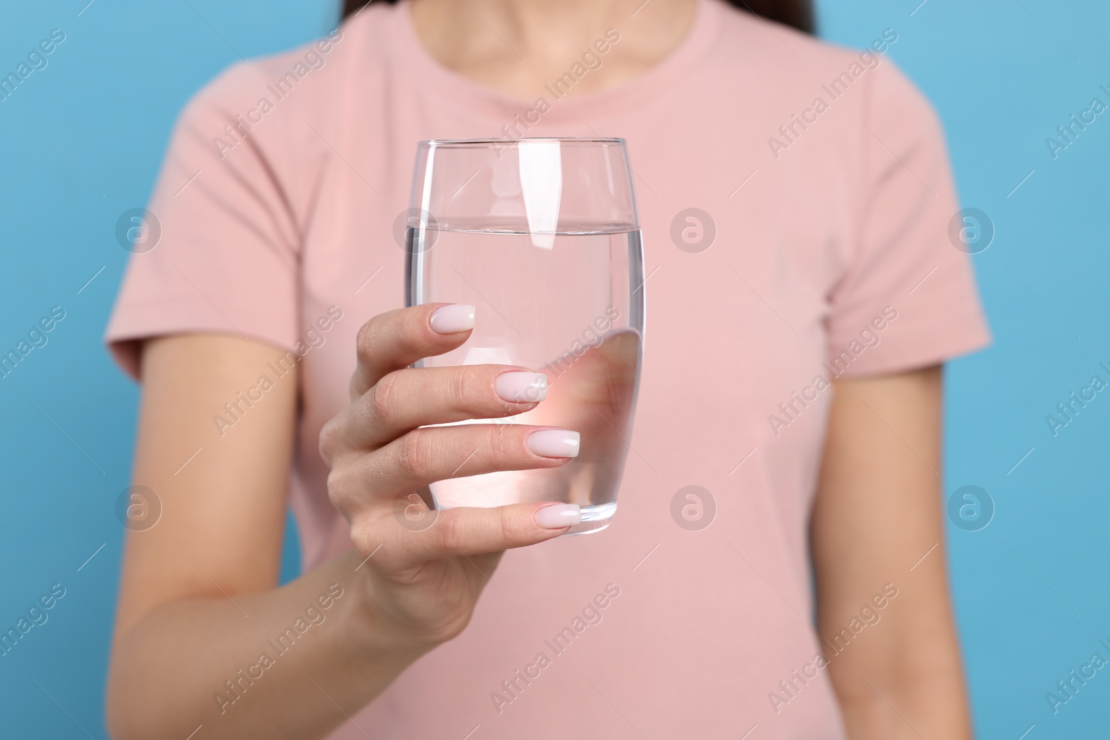 Photo of Healthy habit. Closeup of woman holding glass with fresh water on light blue background