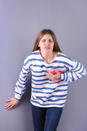 Young woman having heart attack on color background