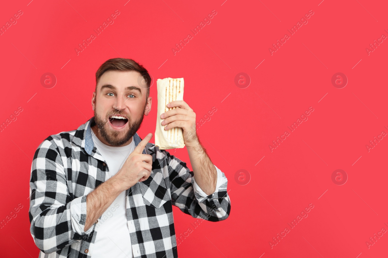 Photo of Excited young man with delicious shawarma on red background, space for text