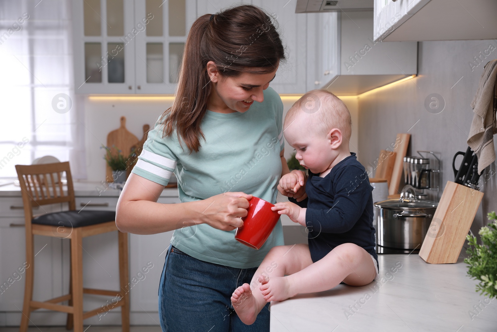 Photo of Happy young woman and her cute little baby spending time together in kitchen