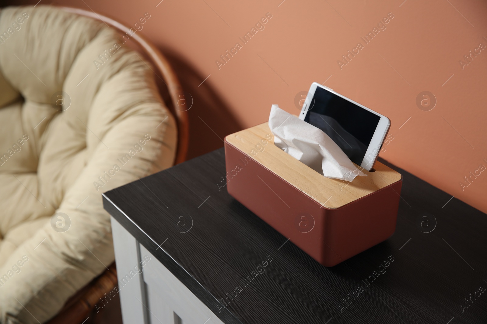 Photo of Box with paper tissues and smartphone on wooden cabinet in room