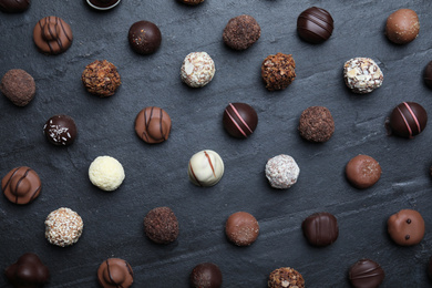 Photo of Different delicious chocolate candies on black table, flat lay