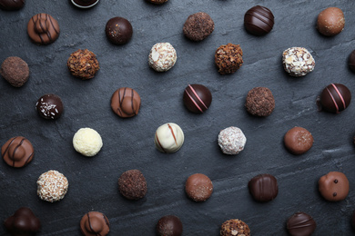 Different delicious chocolate candies on black table, flat lay