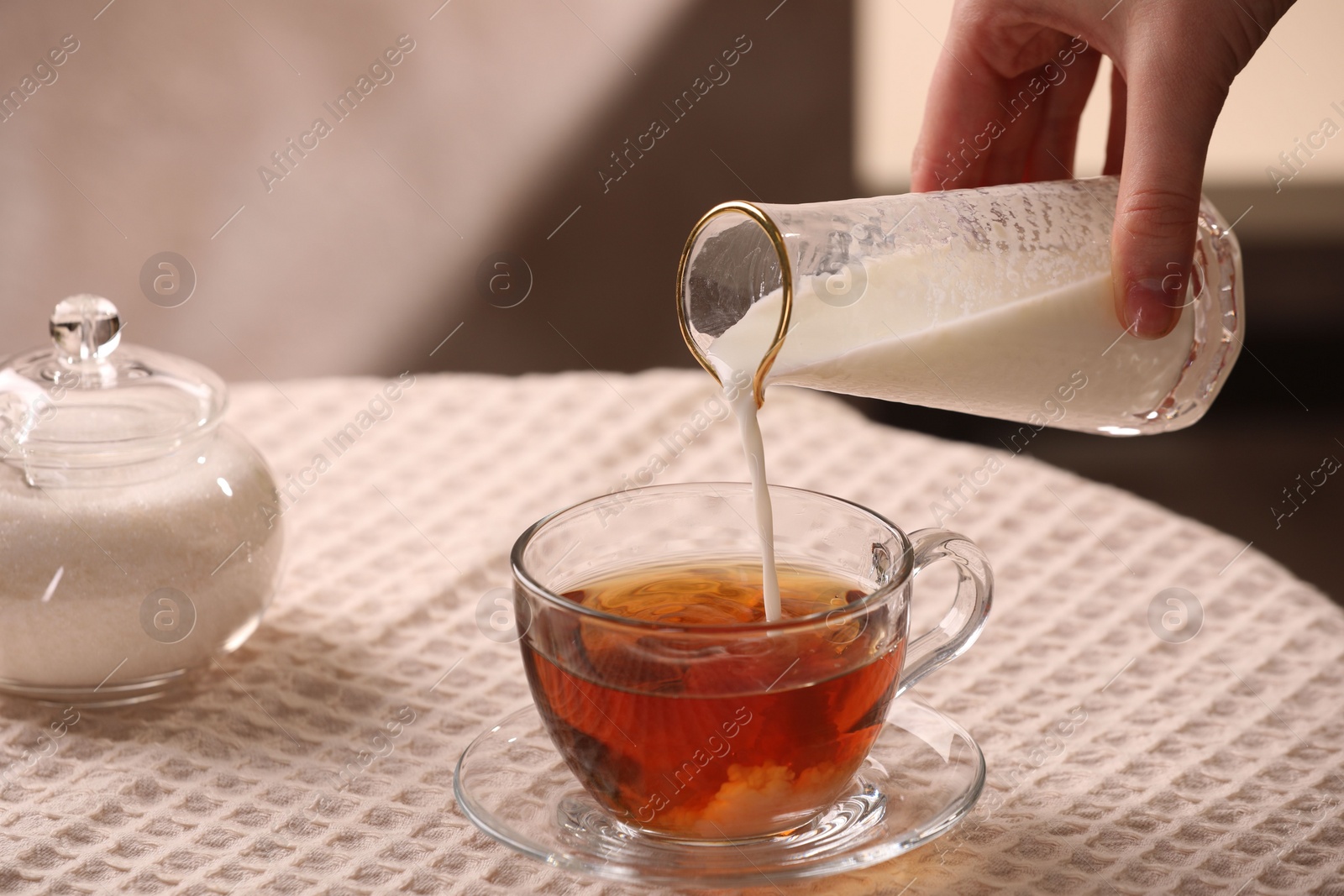 Photo of Woman pouring milk into cup with aromatic tea at table, closeup