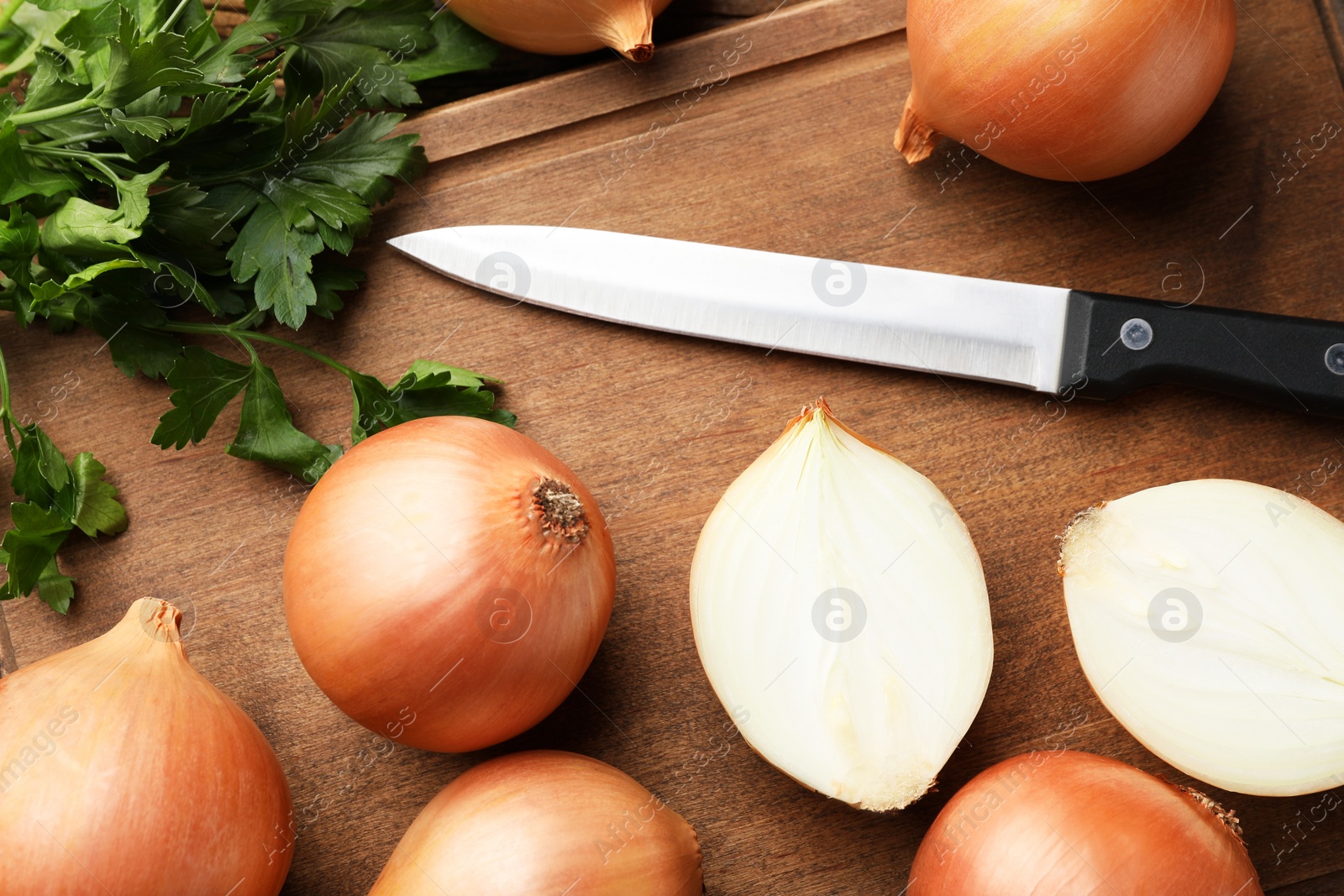 Photo of Whole and cut onions with knife and parsley on wooden table, flat lay