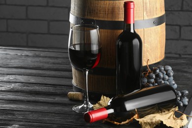 Photo of Delicious wine, wooden barrel, dry leaves and fresh grapes on black table, space for text