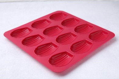Photo of Red baking mold for madeleine cookies on white table, closeup