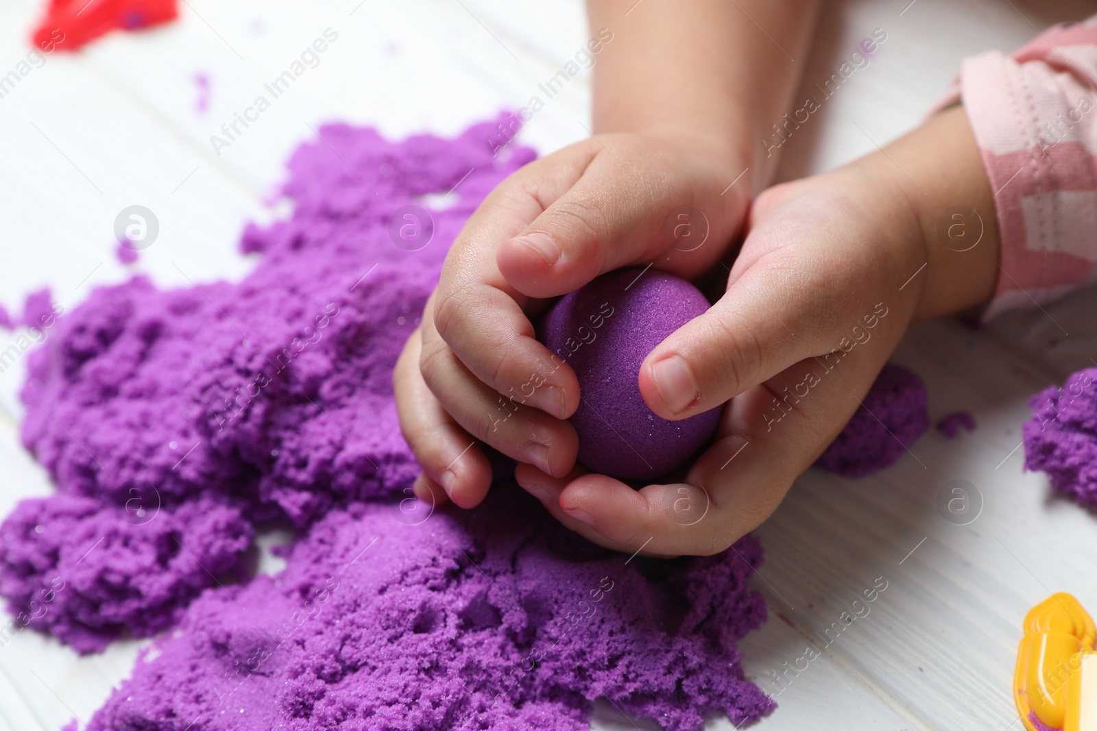 Photo of Little child playing with kinetic sand at white table, closeup