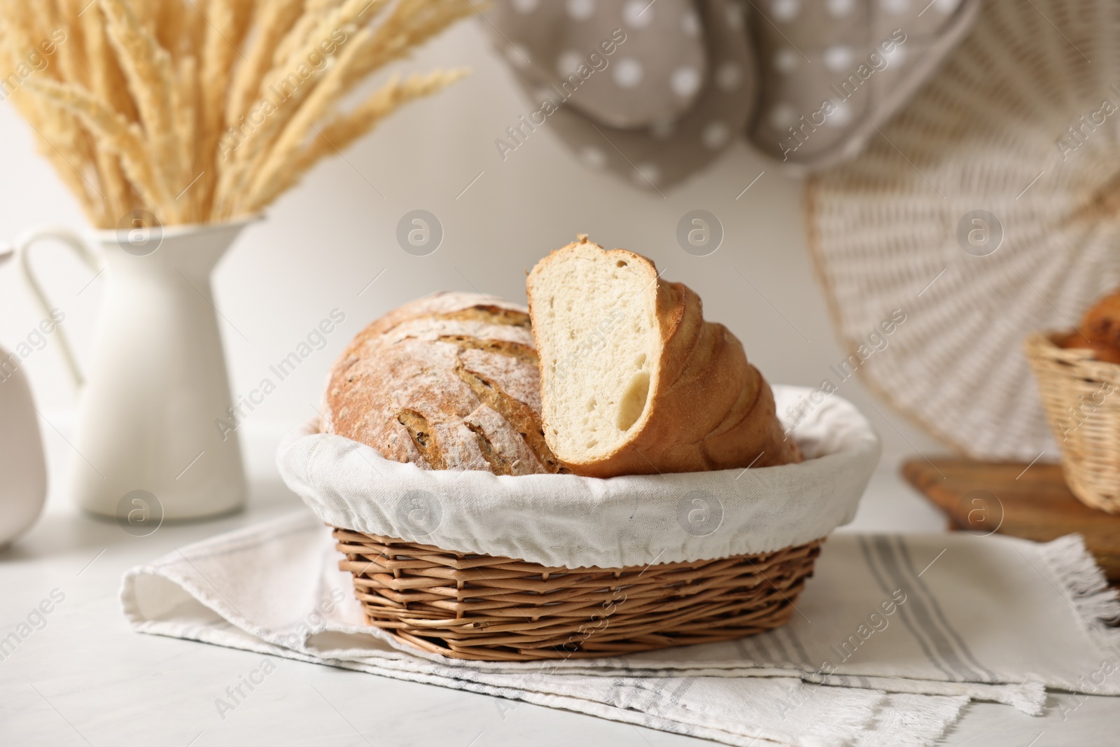 Photo of Wicker bread basket with freshly baked loaf on white marble table in kitchen