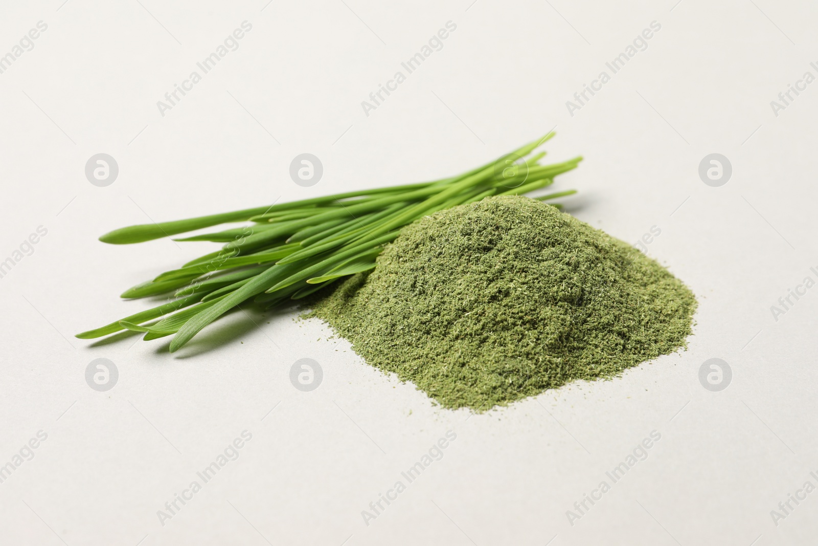 Photo of Pile of wheat grass powder and fresh green sprouts on light table, closeup