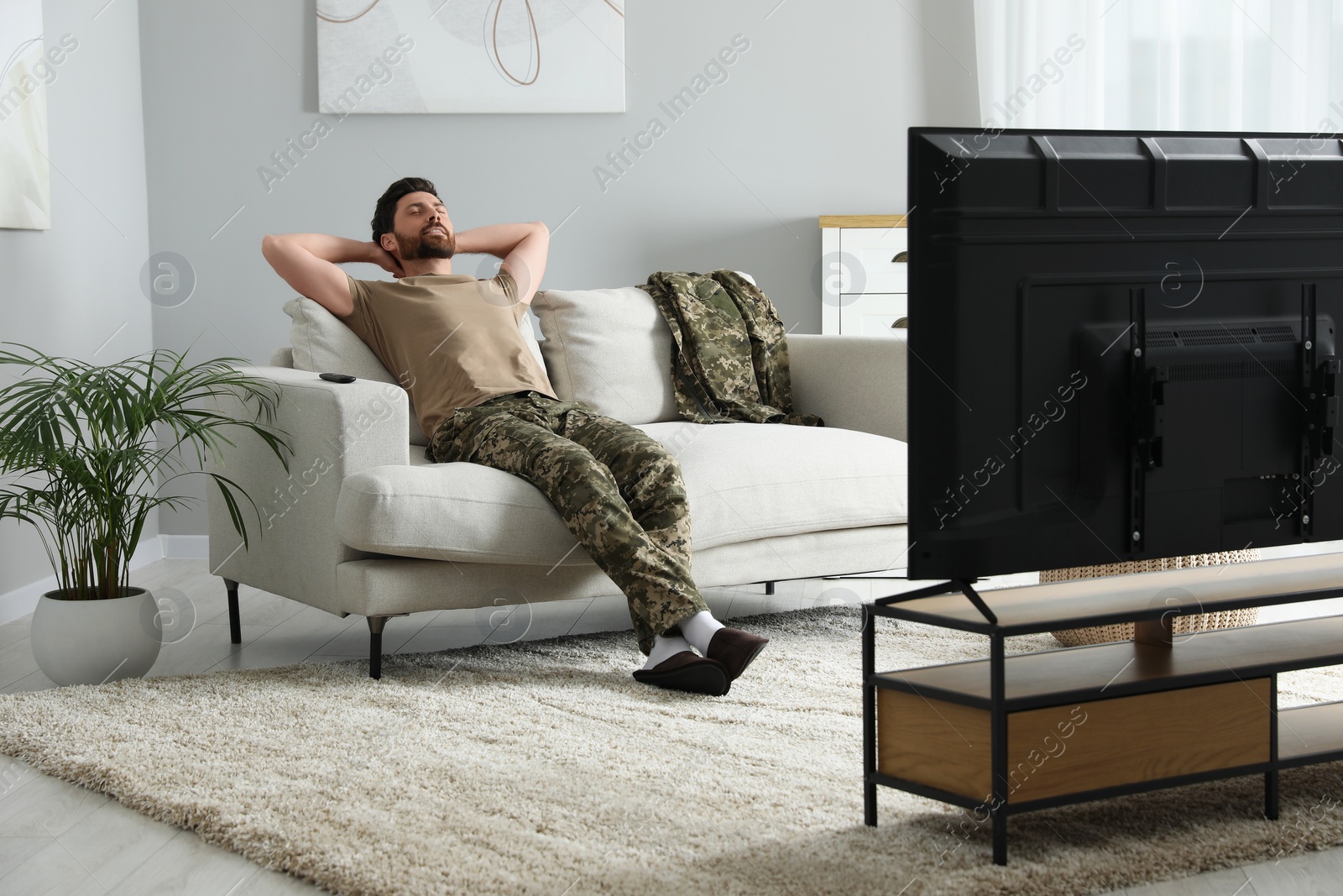 Photo of Soldier napping on soft sofa near TV in living room. Military service