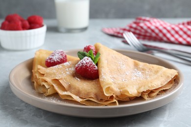 Delicious crepes served with mint, raspberries and powdered sugar on grey table, closeup