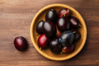 Photo of Tasty ripe plums on wooden table, flat lay