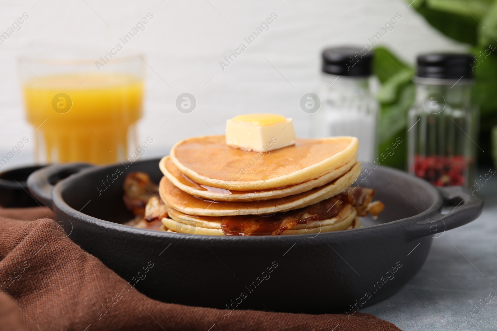 Photo of Tasty pancakes with butter, fried bacon and fresh arugula on grey table, closeup