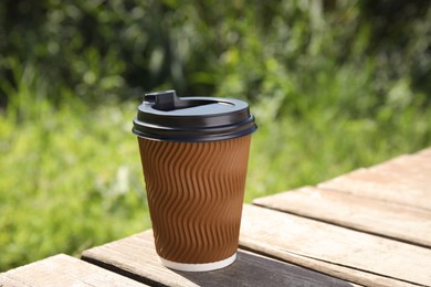 Takeaway cardboard coffee cup with plastic lid on wooden table outdoors