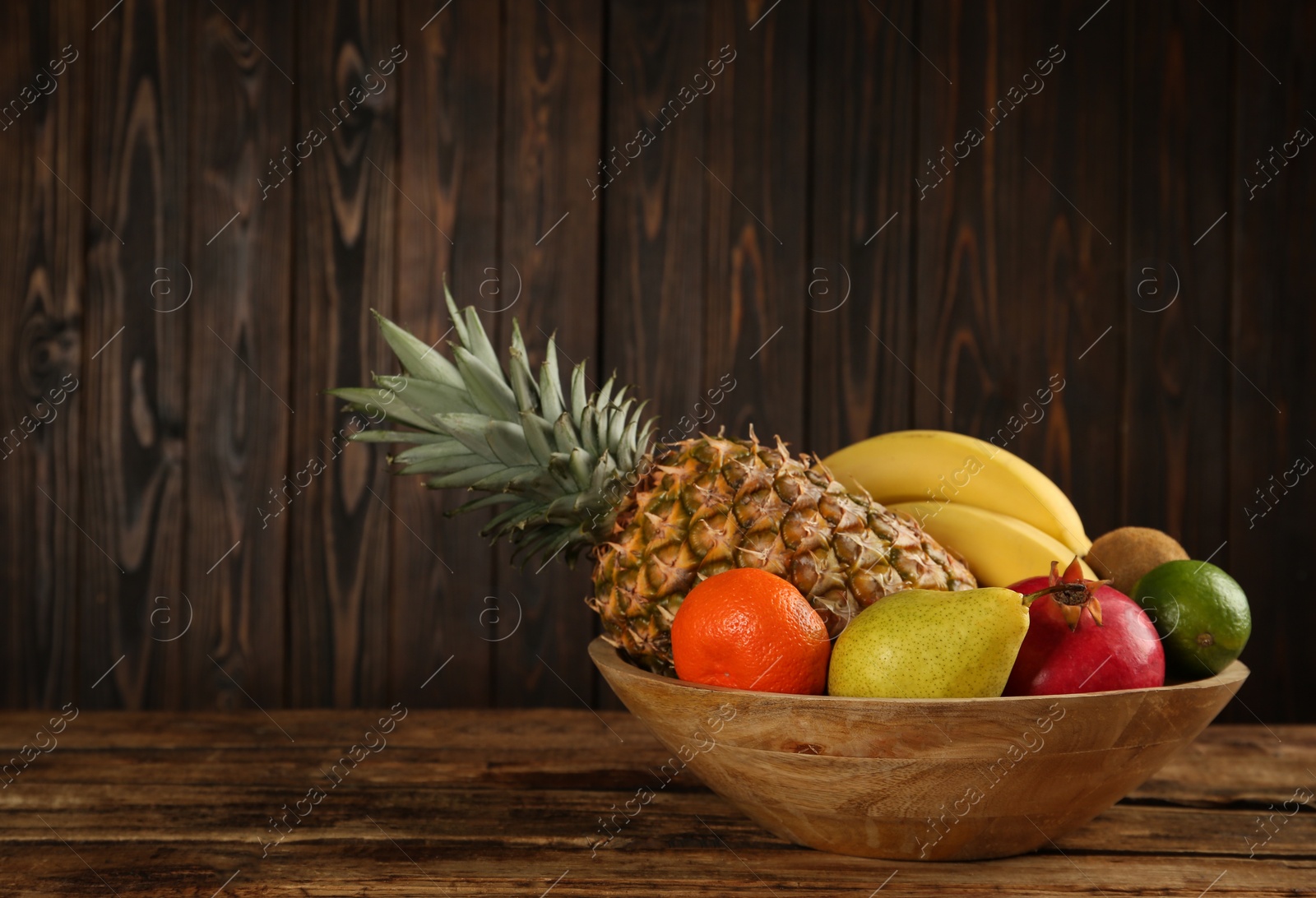 Photo of Fresh ripe fruits in bowl on wooden table, space for text