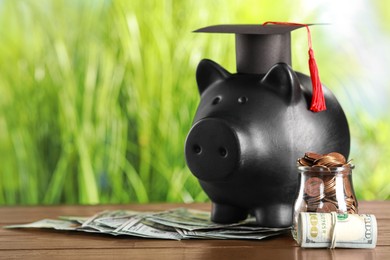 Scholarship concept. Graduation cap, glass jar with coins, dollar banknotes and piggy bank on wooden table, space for text