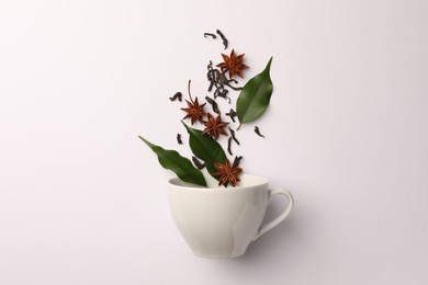 Anise stars, dry tea and green leaves falling into cup on white background, flat lay