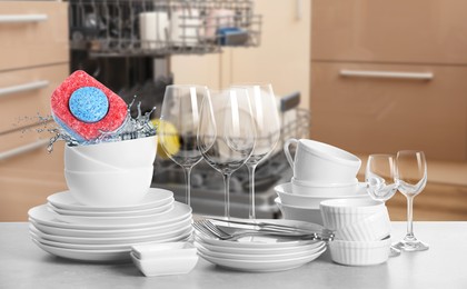 Image of Many clean tableware in kitchen. Dishwasher detergent falling into bowl with water