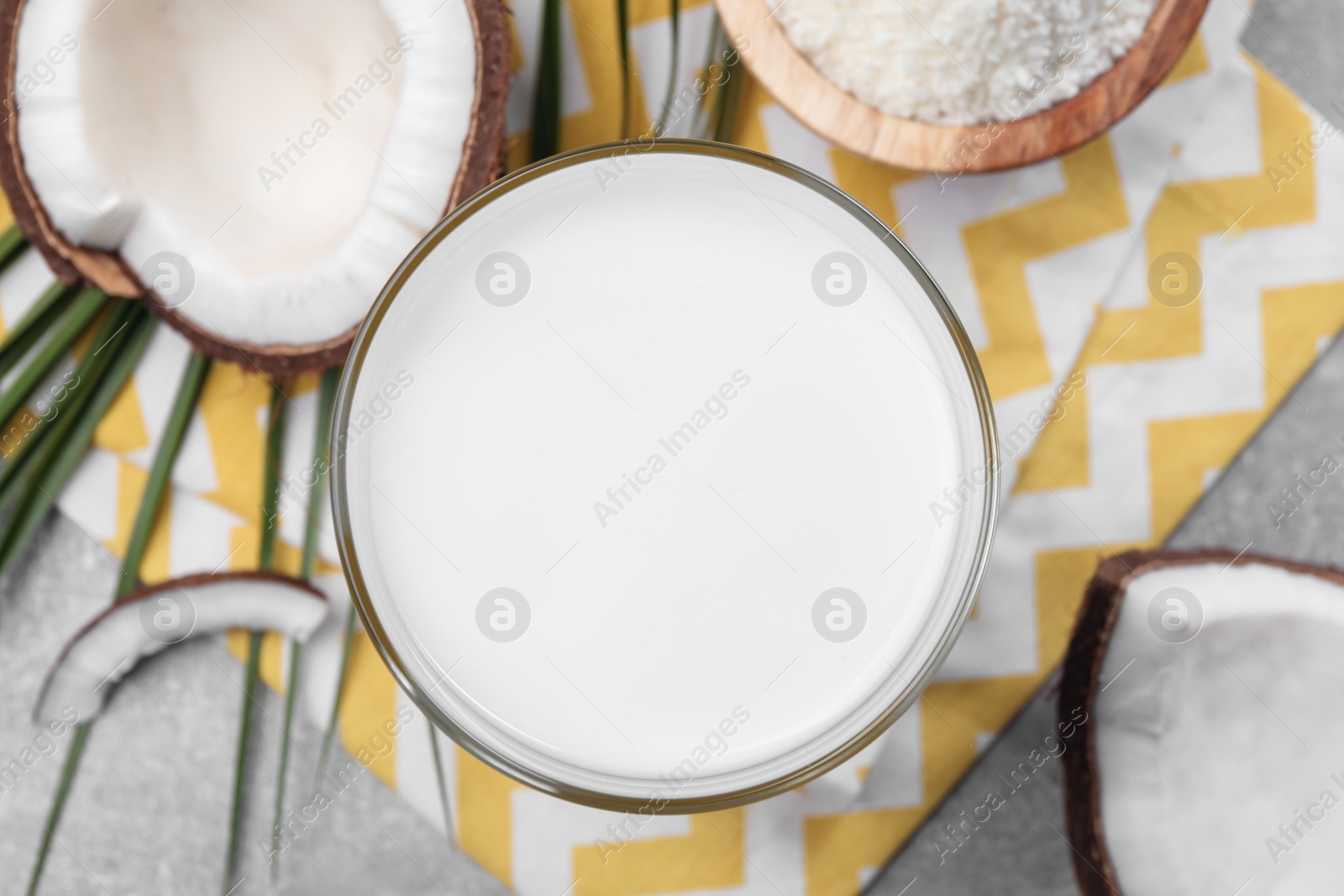 Photo of Glass of delicious coconut milk, flakes and coconuts on light grey table, flat lay