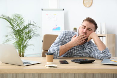 Photo of Lazy young office employee yawning at workplace