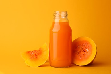Photo of Tasty pumpkin juice in glass bottle and cut pumpkin on orange background