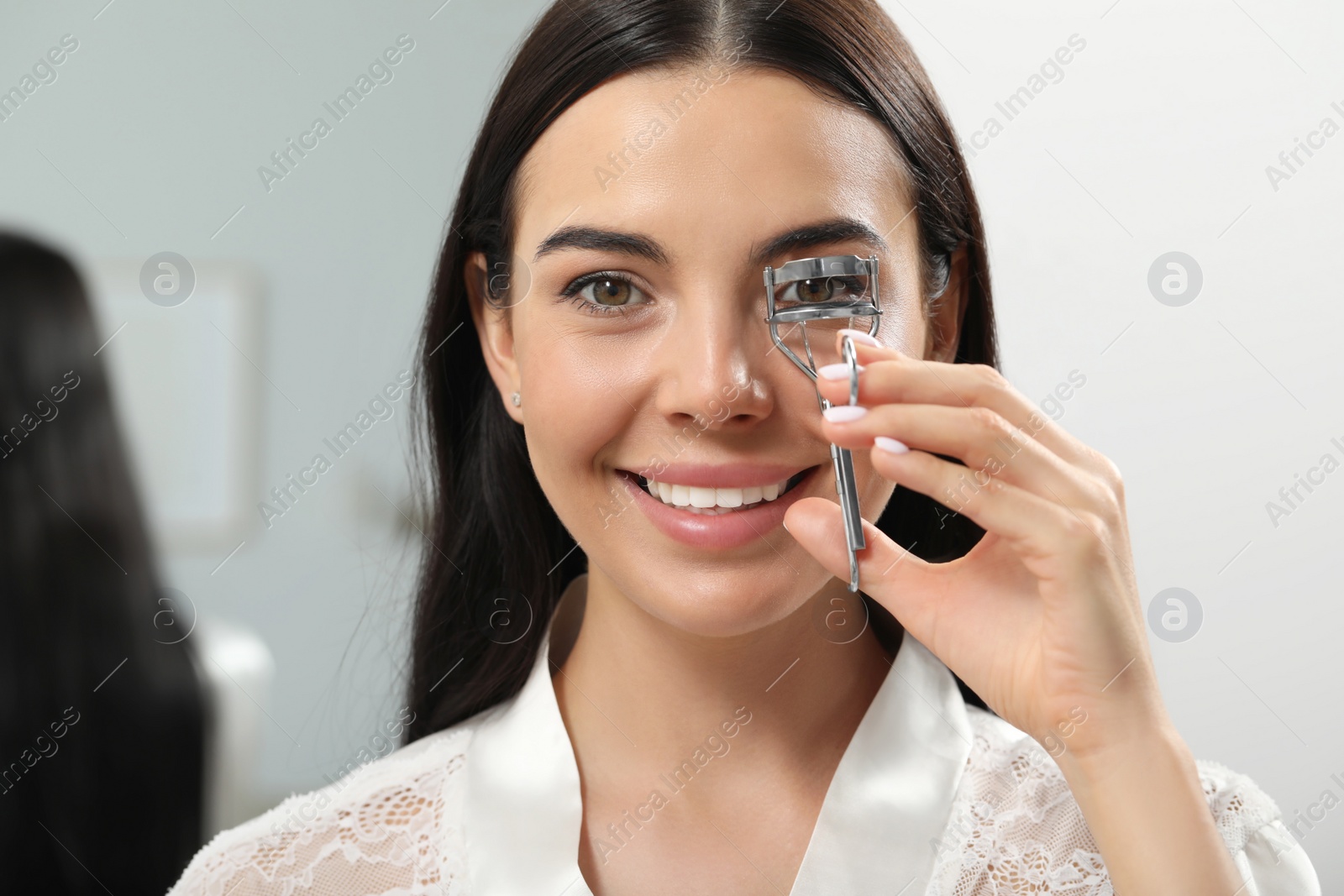 Photo of Beautiful young woman using eyelash curler indoors
