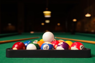 Photo of Plastic triangle rack with billiard balls and cues on green table indoors, space for text