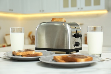Photo of Modern toaster, bread slices with chocolate cream and glasses of milk on white marble table in kitchen