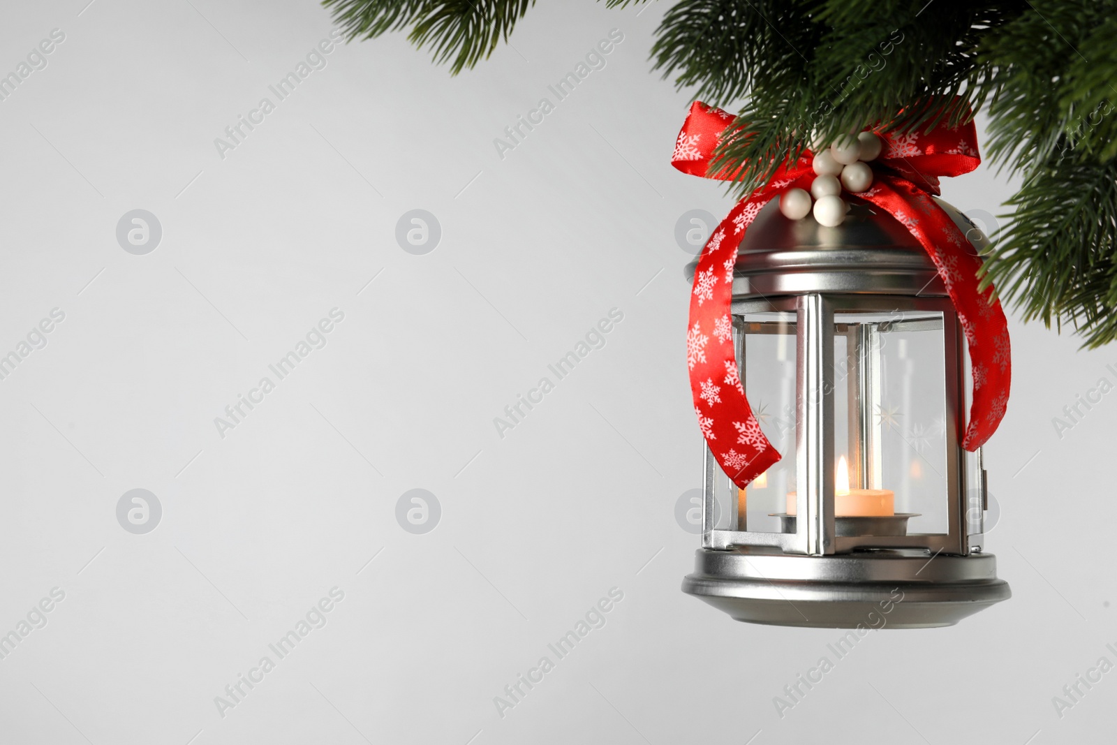 Photo of Vintage Christmas lantern with burning candle hanging on fir branch against light background. Space for text