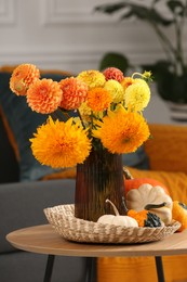 Photo of Beautiful bouquet with bright orange flowers and pumpkins on coffee table indoors. Autumn vibes