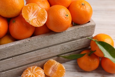 Delicious tangerines with leaves on light wooden table, closeup