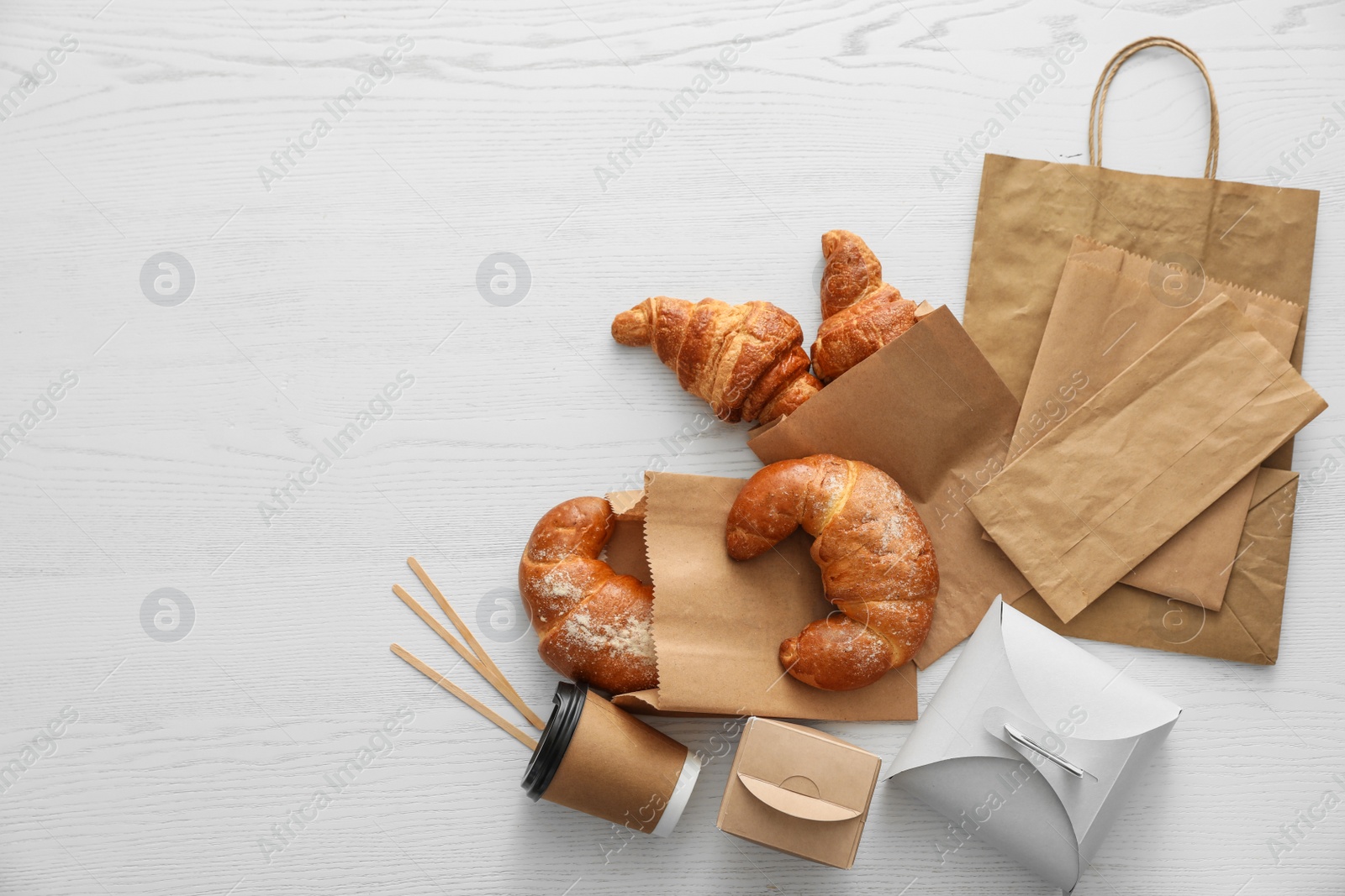 Photo of Flat lay composition with paper bags and pastry on light wooden background. Space for design